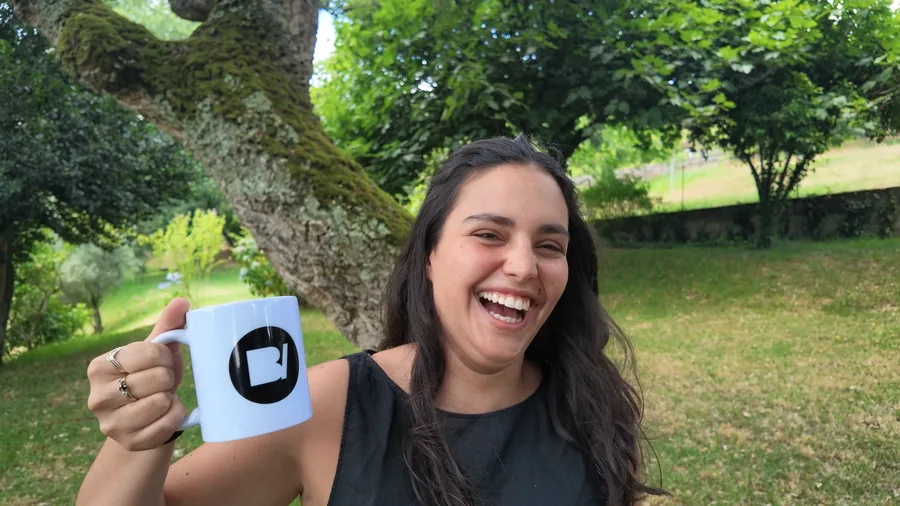 Uma pessoa a rir no jardim, a levantar uma caneca branca com o símbolo da BoldIvy