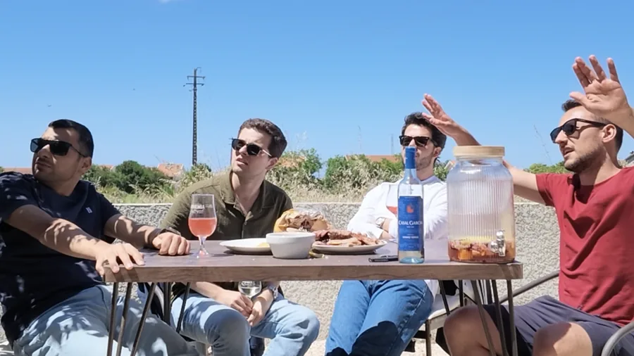 Quatro pessoas à mesa numa esplanada ao sol, com vinho e comida