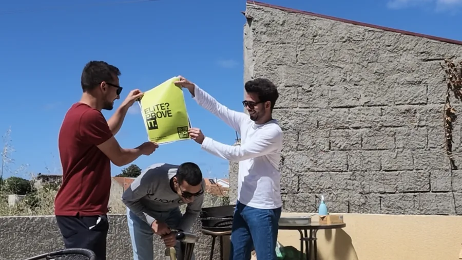 Três pessoas num terraço a segurar um cartaz lima com o lema «Elite? Prove it.»